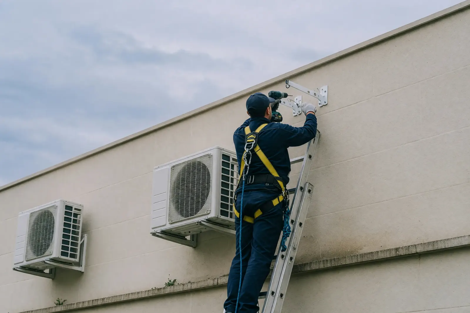 Instalador de aire acondicionado trabajando con arnés en la fachada de un edificio